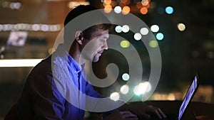 Beautiful businessman working overtime at night in executive office. City lights are visible in background from a large