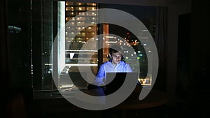 Beautiful businessman working overtime at night in executive office. City lights are visible in background from a large