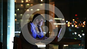 Beautiful businessman working overtime at night in executive office. City lights are visible in background from a large