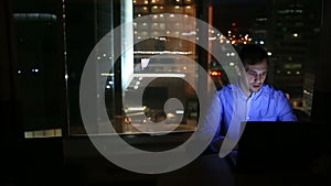 Beautiful businessman working overtime at night in executive office. City lights are visible in background from a large