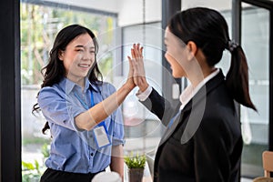 A beautiful businesswoman is giving high fives to her colleague while talking in an office corridor