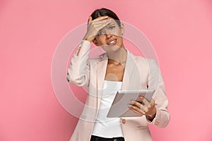 Beautiful businesswoman holding her tablet and slapping her face