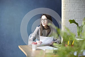 Beautiful businesswoman with long hair working with documentation, sheet, laptop while sitting in modern loft office.