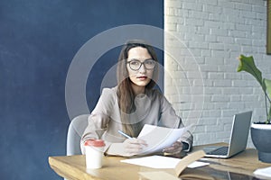 Beautiful businesswoman with long hair working with documentation, sheet, laptop while sitting in modern loft office. photo