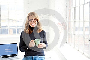 Beautiful businesswoman standing in the office while drinking her coffee photo