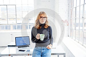 Beautiful businesswoman standing in the office while drinking her coffee photo