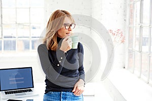 Beautiful businesswoman standing in the office while drinking her coffee