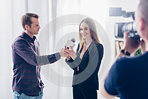 Beautiful businesswoman in suit giving interview to journalist, holding microphone and looking at camera