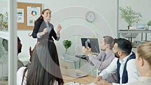 Beautiful businesswoman in suit talking to business team then dancing while colleagues clapping hands