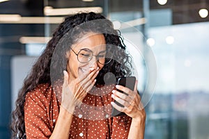 Beautiful businesswoman using phone at workplace, successful and joyful latin american woman typing text message using