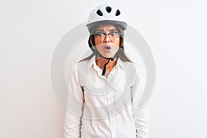 Beautiful businesswoman wearing glasses and bike helmet over isolated white background afraid and shocked with surprise