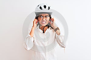 Beautiful businesswoman wearing glasses and bike helmet over isolated white background covering ears with fingers with annoyed