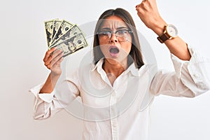 Beautiful businesswoman wearing glasses holding dollars over isolated white background annoyed and frustrated shouting with anger,