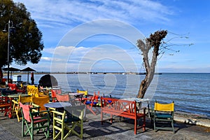 Beautiful cafe on Peraia beach. Colorful chairs and tables in front of blue sea and sky.