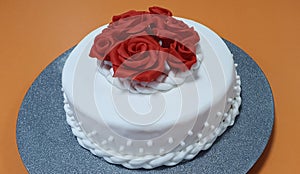 Beautiful cake is covered with white sugarpaste and decorated with red roses