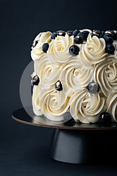 Beautiful cake with white whipped cream cheese curls decorated with blueberries on the black background. Buttercream swirls on the