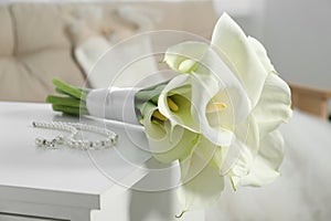 Beautiful calla lily flowers tied with ribbon and jewelry on white chest of drawers indoors, closeup