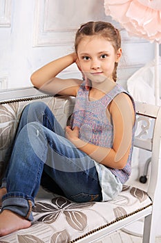 Beautiful calm kid girl sitting on the bench in blue jeans and f