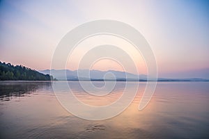 A beautiful, calm morning landscape of lake and mountains in the distance. Colorful summer scenery with mountain lake in dawn.