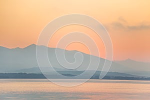 A beautiful, calm morning landscape of lake and mountains in the distance. Colorful summer scenery with mountain lake in dawn.