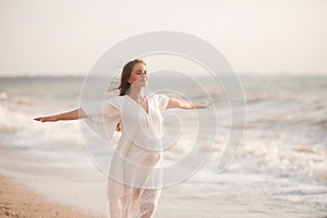 Beautiful calm pregnant woman wear white dress posing over sea at background closeup.