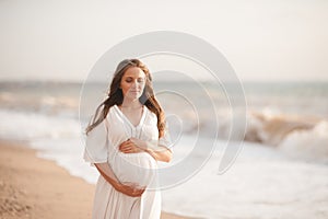 Beautiful calm pregnant woman wear white dress posing over sea at background closeup.