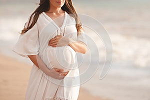 Beautiful calm pregnant woman wear white dress posing over sea at background closeup.