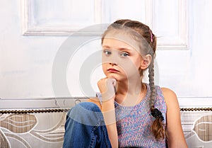 Beautiful calm thinking unhappy kid girl sitting on the bench in