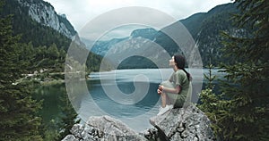 Beautiful calm woman sitting on rock coastline. Girl having moment alone, uniting with nature and enjoying life