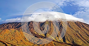 Beautiful canarian wild landscape, rugged volcano cone Pico del Teide with white smooth fluffy pileus cloud cover hat,  Tenerife