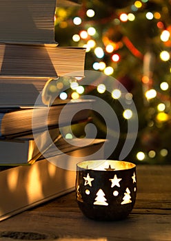 Beautiful candle on a wooden table with a stack of books and christmas garlands on the background