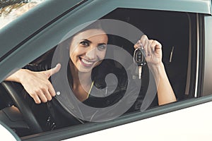 Beautiful car driver woman smiling showing new car keys and car. Caucasian girl sitting in automobile, smiling and