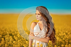 Beautiful carefree girl with long curly healthy hair over Yellow rape field landscape background. Attracive brunette with blowing