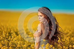 Beautiful carefree girl with long curly healthy hair over Yellow rape field landscape background. Attracive brunette with blowing