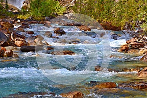 Beautiful cascade mountains stream. Blue river, brown stones in the water, green bushes on the shore.