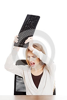 Beautiful casual woman behind the desk trying to broke the keyboard.