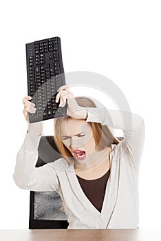 Beautiful casual woman behind the desk trying to broke the keyboard.