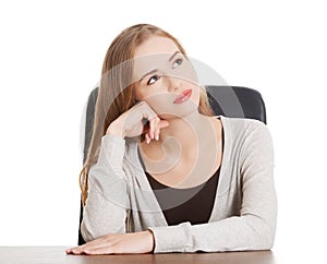 Beautiful casual woman sitting by a desk and day- dreaming.