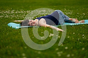 Beautiful caucaisan young woman working out outdoors on blue mat. Jathara Parivartanasana top view