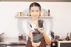 Beautiful caucasian barista woman gives takeaway coffee cups in one hand forward and show one takeaway coffee cup in another hand