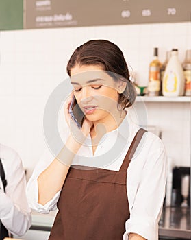 Beautiful caucasian barista woman receiving online coffee orders from customer via mobile phone for takeaway coffee cup from cafe