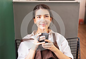 Beautiful caucasian barista woman sitting blankly and enjoys hot black coffee in coffee break at coffee shop