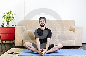 Beautiful caucasian bearded man in black clothes on blue yogamat doing gracious posture with closed eyes