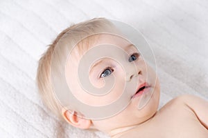 Beautiful caucasian blonde baby girl, infant lying on bed. Happy childhood, baby care concept, close-up