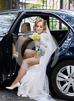 Beautiful caucasian blonde bride sitting in a stylish car with a bouquet