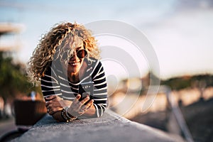 Beautiful caucasian blonde curly woman lay down outdoor and use cellular mobbile phone sending messages and reading internet