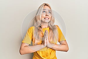 Beautiful caucasian blonde girl wearing casual tshirt begging and praying with hands together with hope expression on face very