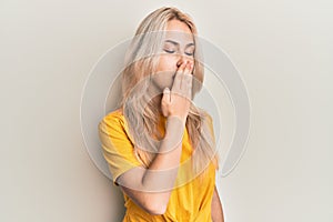 Beautiful caucasian blonde girl wearing casual tshirt bored yawning tired covering mouth with hand