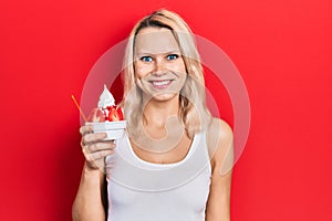 Beautiful caucasian blonde woman eating strawberry ice cream looking positive and happy standing and smiling with a confident