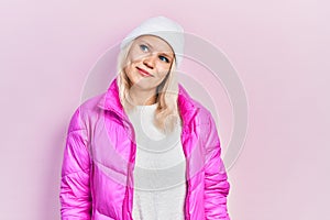 Beautiful caucasian blonde woman wearing wool hat and winter coat looking away to side with smile on face, natural expression